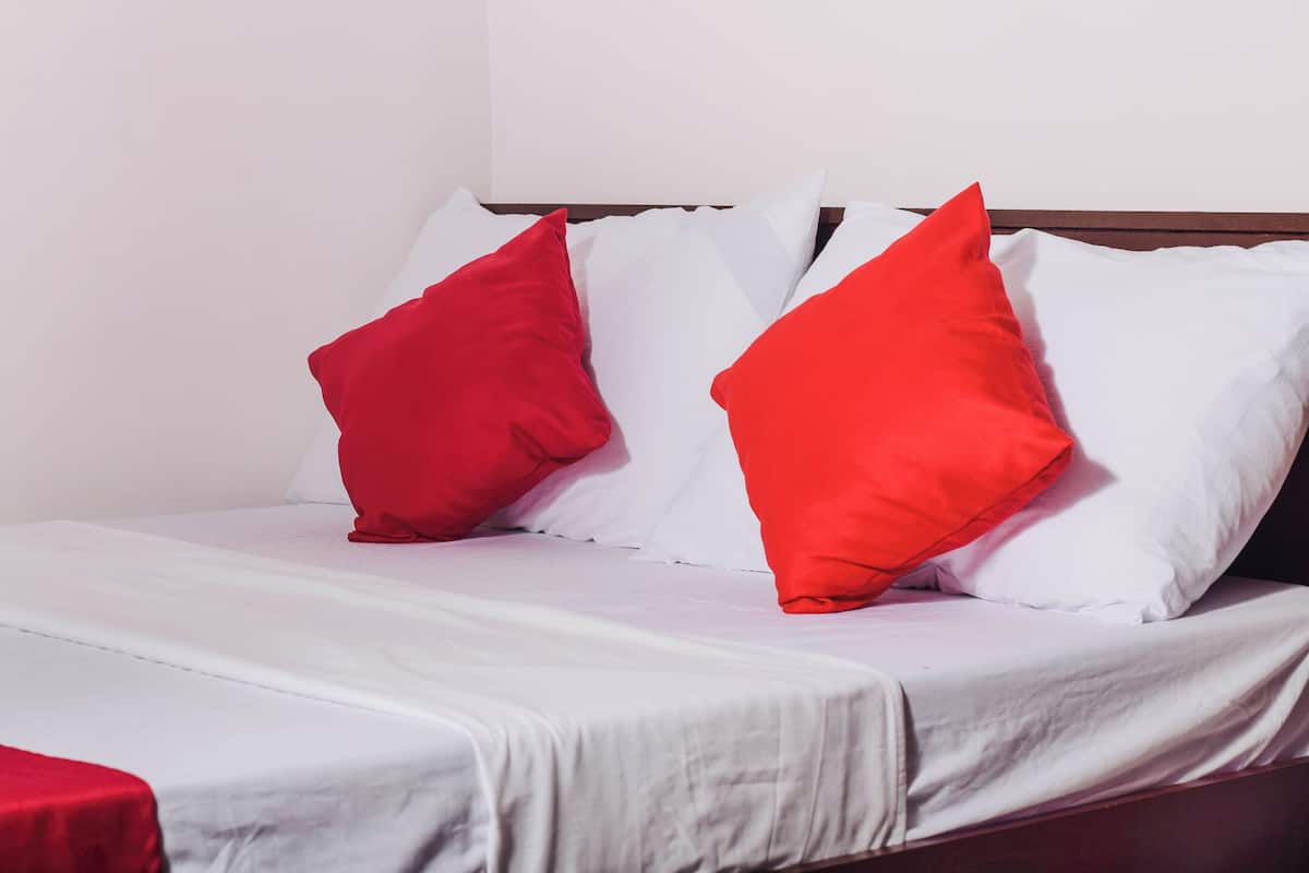 A bed with white bedding and two red pillows.
