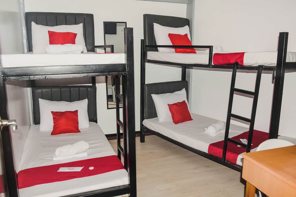 A dormitory room with bunk beds, each with a white mattress and red pillows.