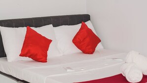 Cama bem arrumada com travesseiros brancos e vermelhos, manta branca e toalha branca enrolada.