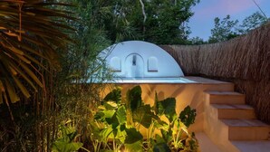 A modern outdoor kitchen with a curved white structure, surrounded by lush greenery and a thatched wall. - Villa Sanah 12 con alberca privada ubicada en Tulum (Tulum)