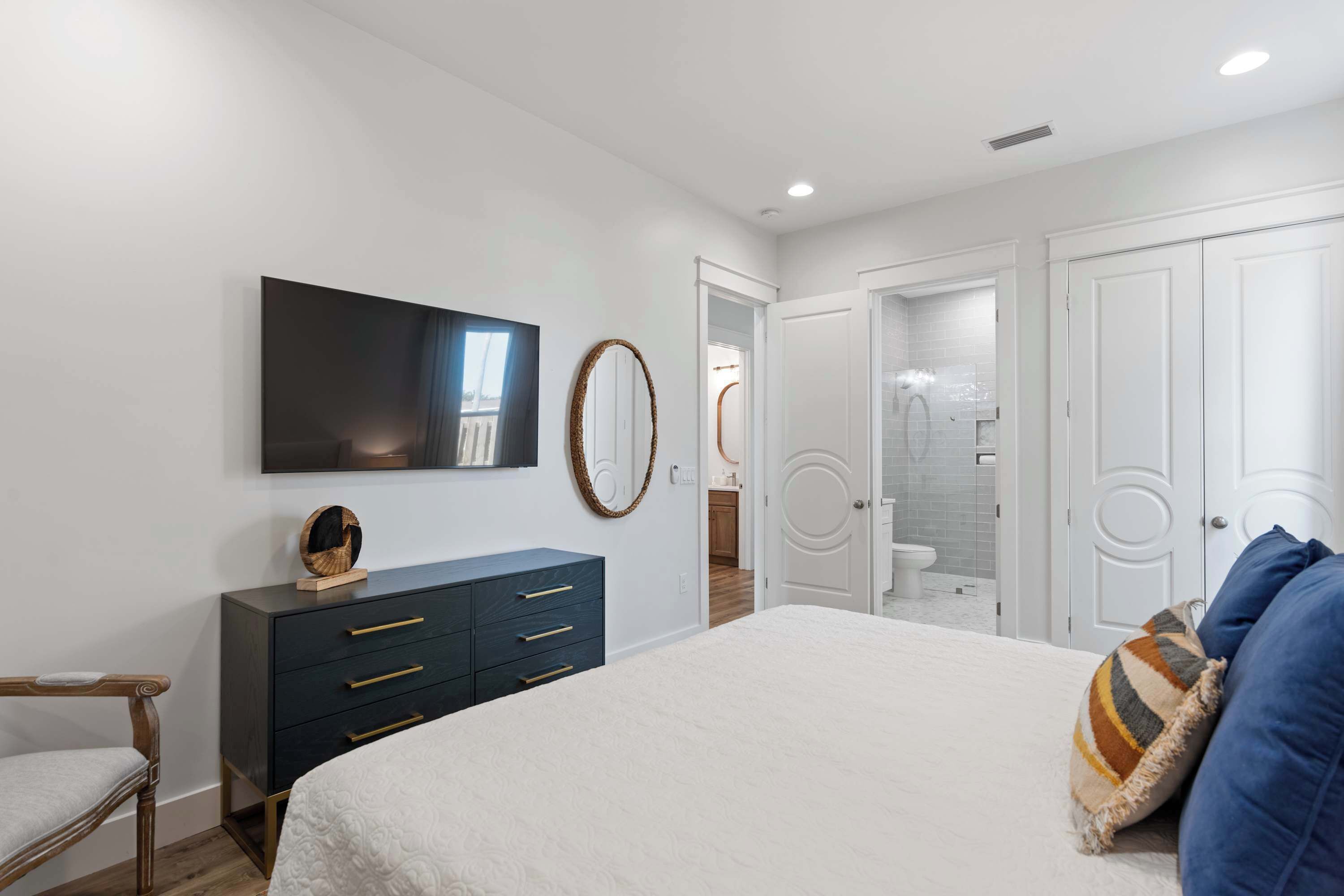 Quarto com cama, cômoda, televisão, espelho e porta para um banheiro.