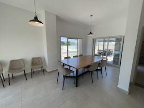 A spacious dining area with a large wooden table and six chairs, two pendant lights, and a sliding glass door leading to an outdoor patio. - Splendid, Modern, and Cozy With Pool (Buenos Aires)