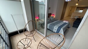 A balcony with two wicker chairs, a bed with patterned bedding, a small table, and a lamp. - Splendid, Modern, and Cozy With Pool (Buenos Aires)