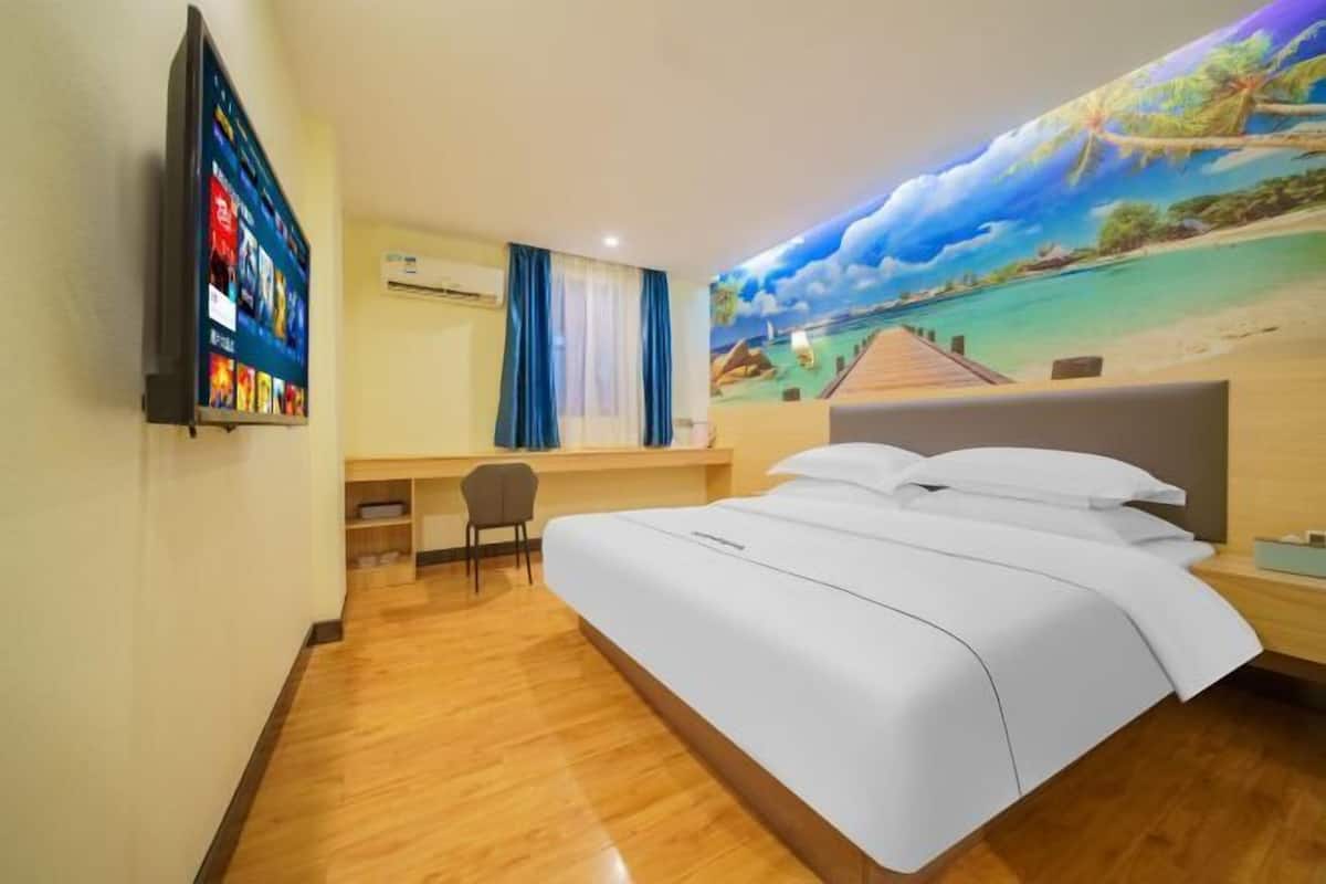 A hotel room with a bed, a desk, a chair, a TV, and a mural of a beach scene.