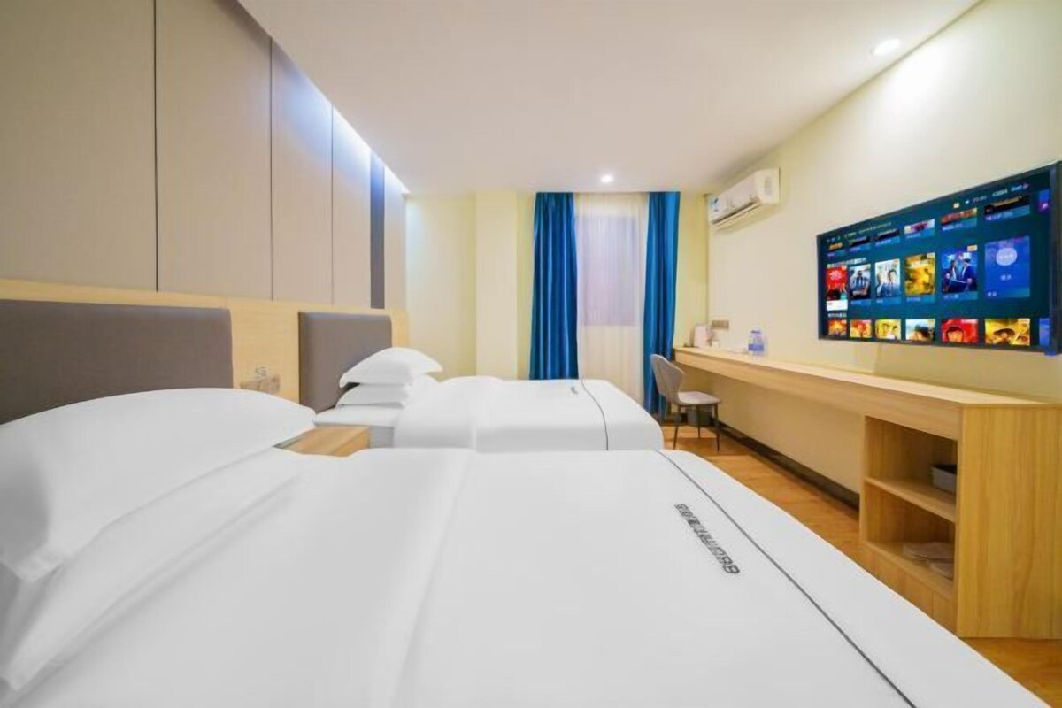 A hotel room with two beds, a desk, a TV, and a window with curtains.