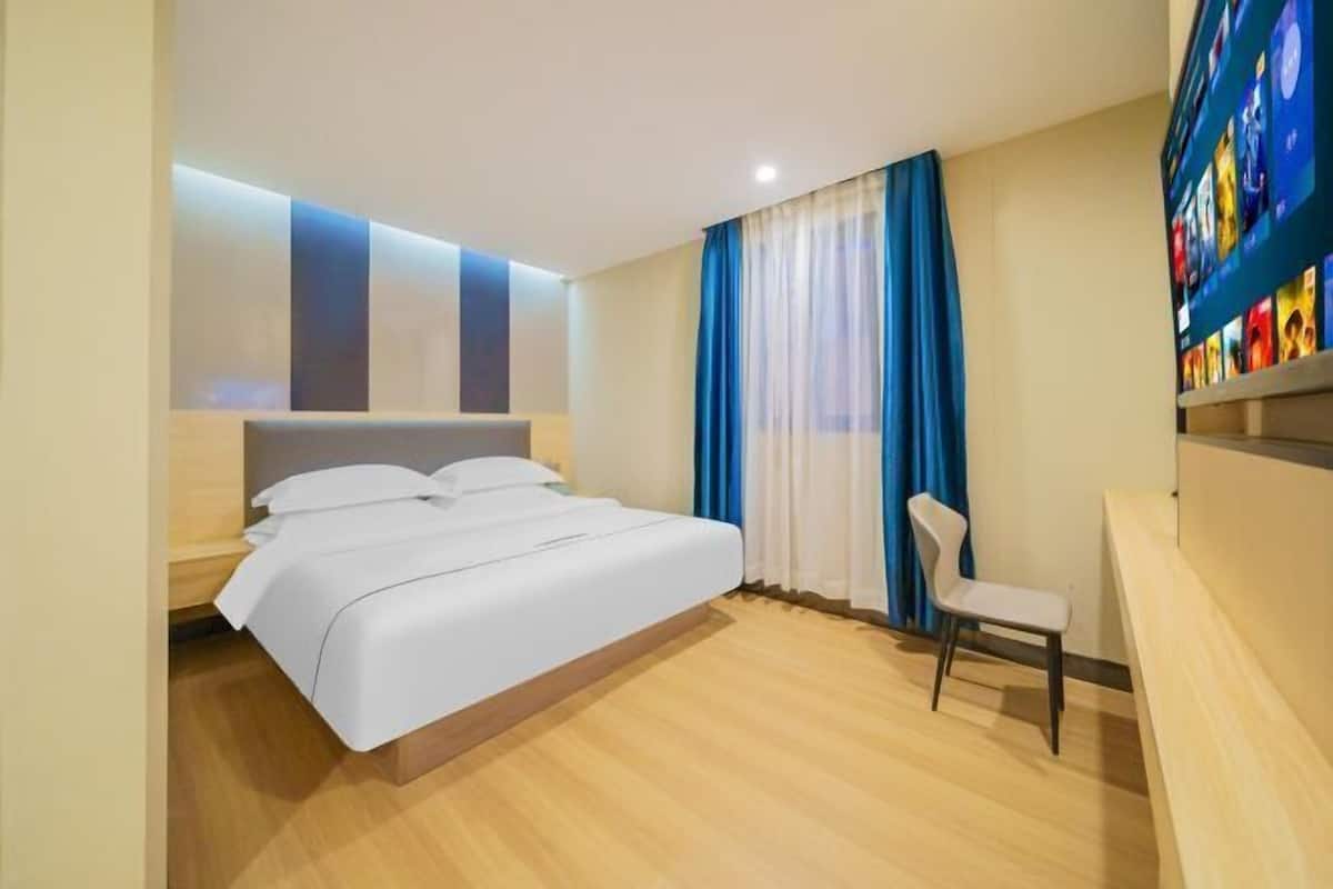 A hotel room with a bed, a chair, a TV, and a bookshelf.