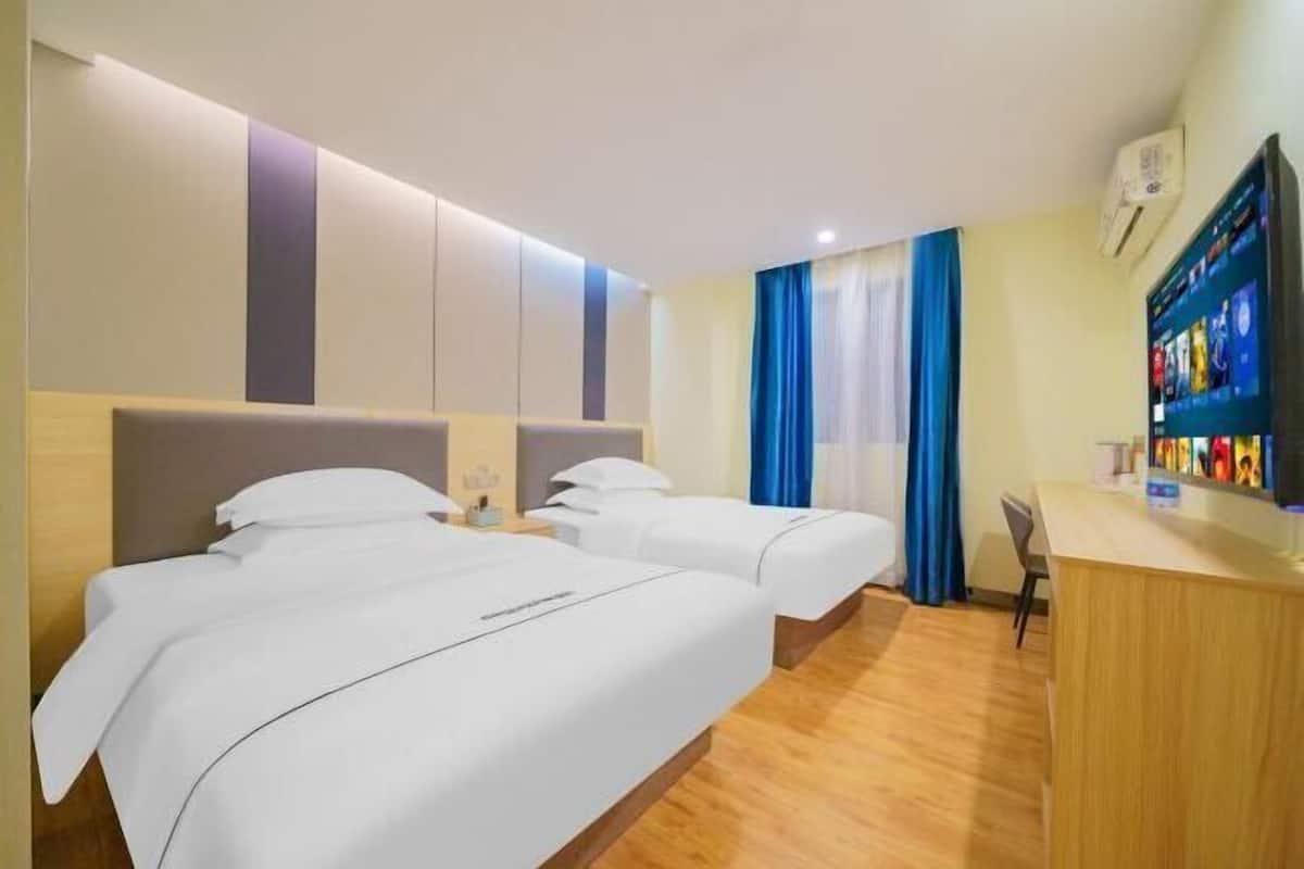 A hotel room with two beds, a desk, and a TV.