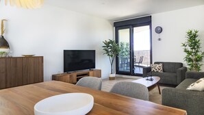 A modern living room with a wooden dining table, grey sofas, a flat-screen TV, and a sliding glass door leading to an outdoor balcony. - Cubo's Urban Sky Apartment Malaga View 17 / urban / air conditioning / free wifi / community pool (Málaga)