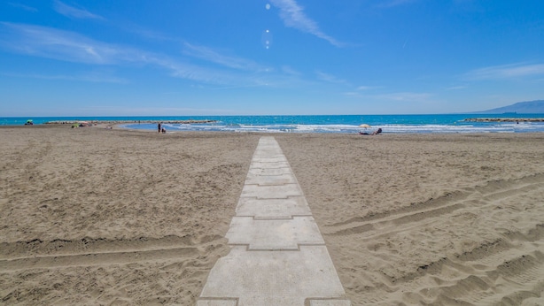 Une plage avec un ciel dégagé et une promenade dallée qui mène à l’eau.