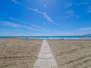 A beach with a clear sky and a paved walkway leading to the water.