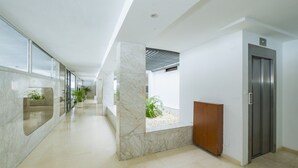 Un couloir moderne avec un sol en marbre, un meuble en bois et une porte d’ascenseur en métal.
