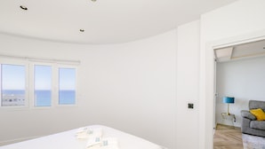 A bedroom with a bed, a view of the sea through three windows, and a grey sofa in the adjacent room. - Cubo's Vistalmar Calahonda Apartment / beach access / terrace / communal pool / free wifi (Mijas Costa)