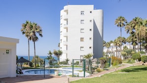 A pool area with a clear view of the ocean, surrounded by palm trees and a white building with multiple balconies. - Cubo's Vistalmar Calahonda Apartment / beach access / terrace / communal pool / free wifi (Mijas Costa)