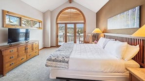Une chambre avec un grand lit, une commode en bois, une télévision et des œuvres d’art accrochées au mur.