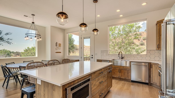 Una cocina moderna con una isla grande, armarios de madera, electrodomésticos de acero inoxidable e iluminación colgante.