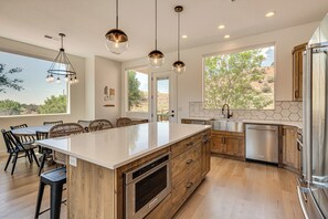 Une cuisine moderne dotée d’un grand îlot central, de meubles en bois, d’appareils électroménagers en acier inoxydable et de luminaires suspendus.