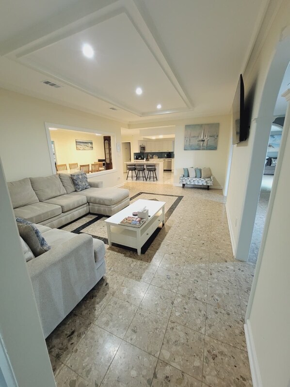 A spacious living room with a sectional sofa, a coffee table, and a kitchen in the background.