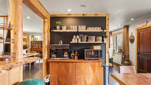 Un coin bar en bois équipé d’un four à micro-ondes, d’une machine à café et d’étagères où sont rangés de la verrerie et des assiettes.