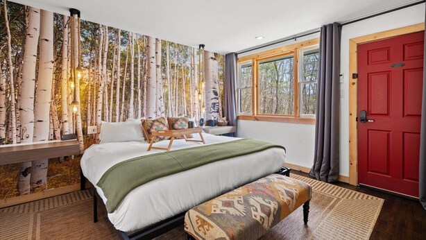 Une chambre à coucher avec un grand lit, un banc, une fenêtre avec des rideaux et une porte rouge.
