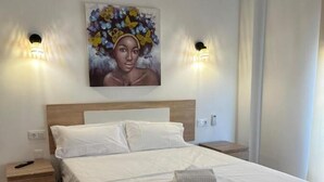 A neatly made bed with white linens and a folded towel, a wooden nightstand with a remote control, and a painting of butterflies on the wall. - Hotel Key Reig (Almussafes)