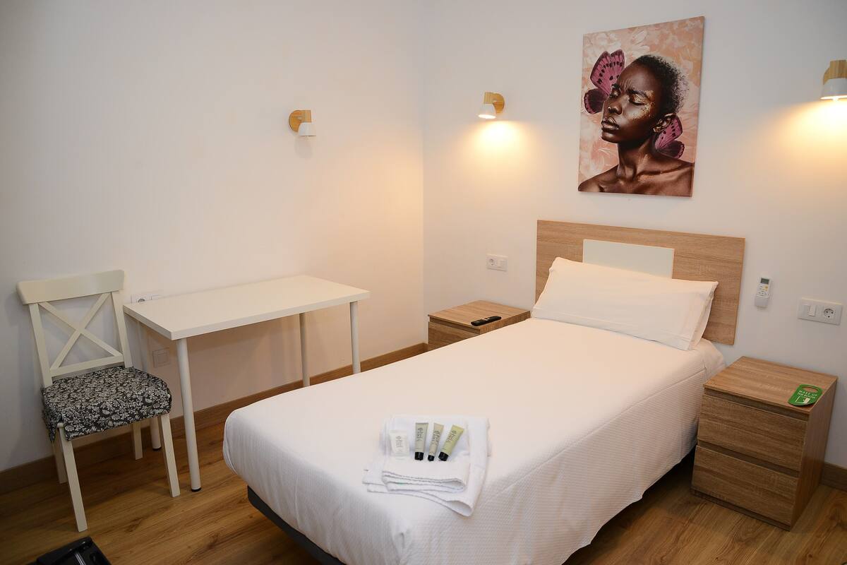 A neatly arranged hotel room with a bed, a desk, a chair, and a nightstand.