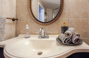 Une salle de bain avec un lavabo blanc, un miroir à cadre doré, un distributeur de savon et un porte-serviettes avec des serviettes.