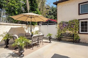 Une terrasse extérieure avec une table et des chaises, un grand parasol et des plantes en pot.