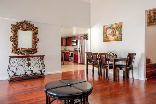 Un vaste espace de vie comprenant une table et des chaises, un parquet, un miroir décoratif et une cuisine à l’arrière-plan.