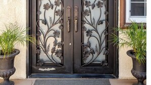 Een dubbele deur met ingewikkeld metaalwerk en twee handgrepen, omzoomd door potplanten.