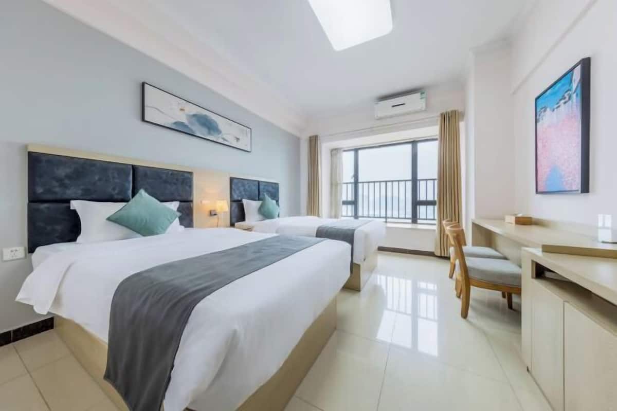 Quarto de hotel com duas camas, uma escrivaninha, uma cadeira, uma janela ampla com vista e obras de arte nas paredes.