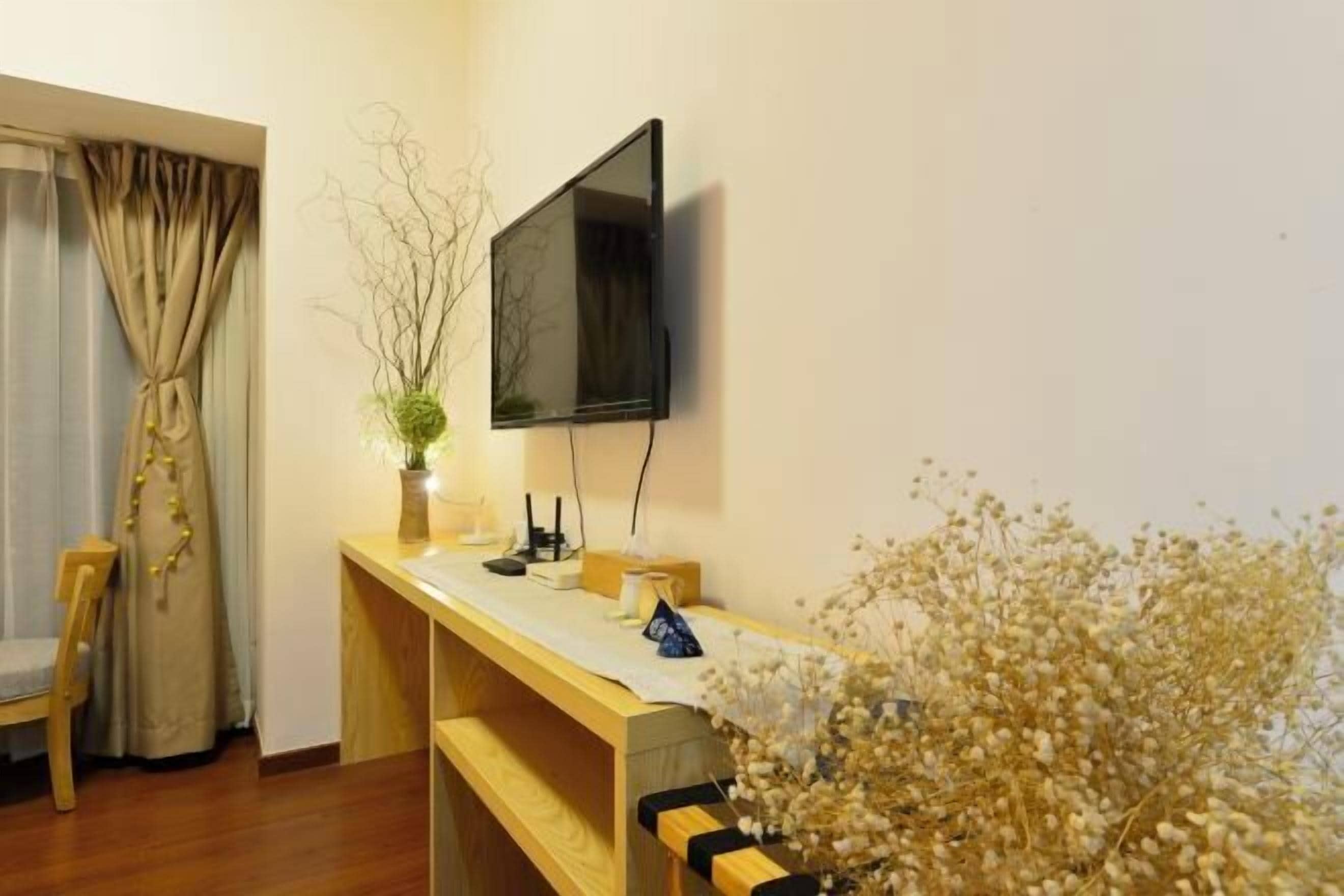 Une pièce avec un bureau en bois, un téléviseur à écran plat fixé au mur, une chaise et une fenêtre avec des rideaux.