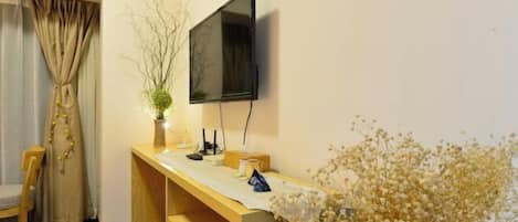 Una habitación con un escritorio de madera, un televisor de pantalla plana montado en la pared, una silla y una ventana con cortinas.