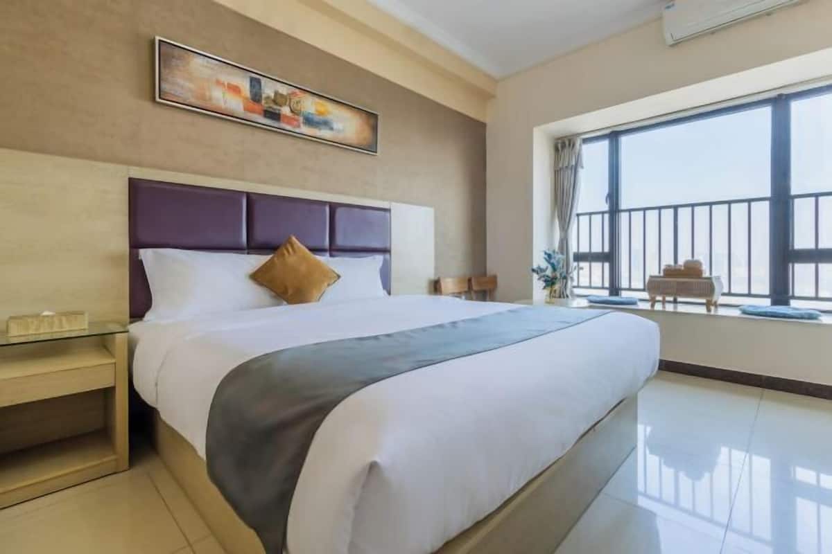 Quarto de hotel com uma cama grande, mesa de cabeceira, pintura na parede e vista pela janela.