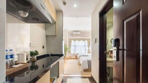 Eine moderne Küche mit schwarzem Arbeitsplatz, integriertem Herd und Spüle. Ein Flur führt zu einem Schlafzimmer mit Bett und Fenster.