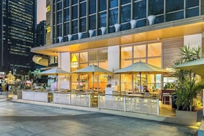 A modern hotel with outdoor seating, large windows, and a well-lit entrance. - Xizhengjia Apartment (Guangzhou Pazhou Exhibition Wanshengwei Subway Station Branch) (Guangzhou)