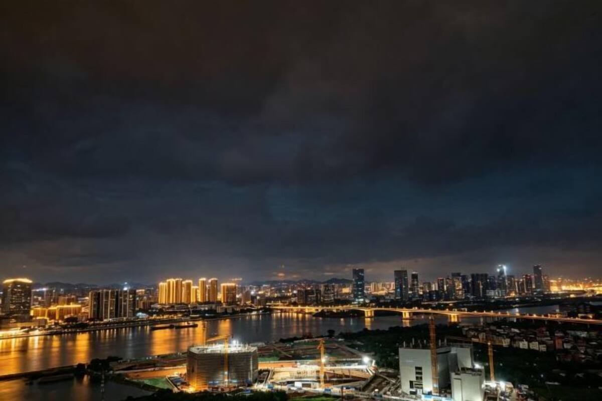 Paisagem urbana noturna com rio, edifícios iluminados e uma ponte.