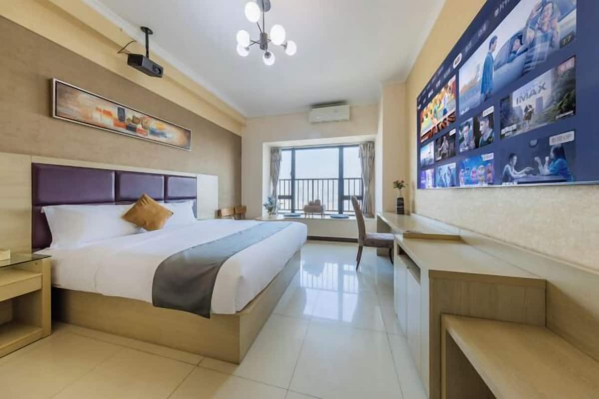 Quarto de hotel moderno com uma cama grande, uma mesa de trabalho e uma parede decorada com cartazes de filmes.