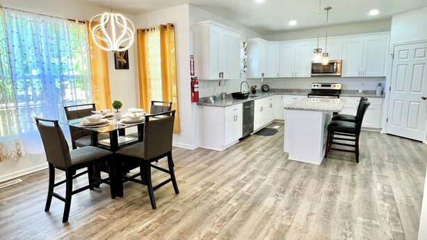 A modern kitchen with white cabinets, a central island, and a dining area with a table and chairs.