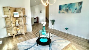 A modern living room with a wooden floor, a glass coffee table, and a hanging light fixture.