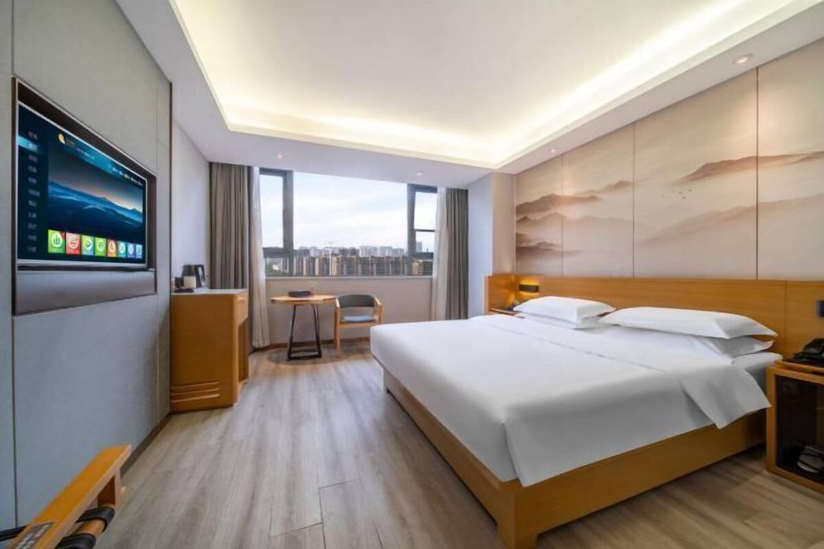 Una habitación de hotel con cama, escritorio, televisor y vistas a la ciudad.