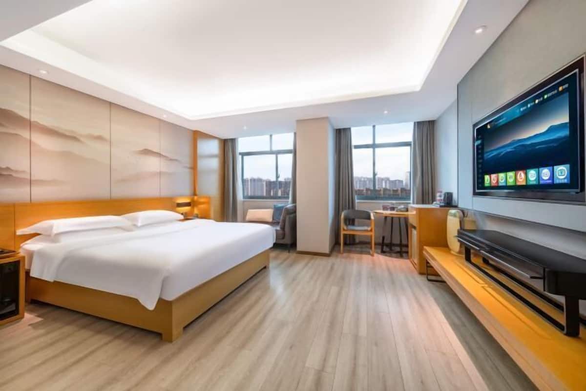 Habitación de hotel con cama, escritorio, silla, televisión y vistas a la ciudad.