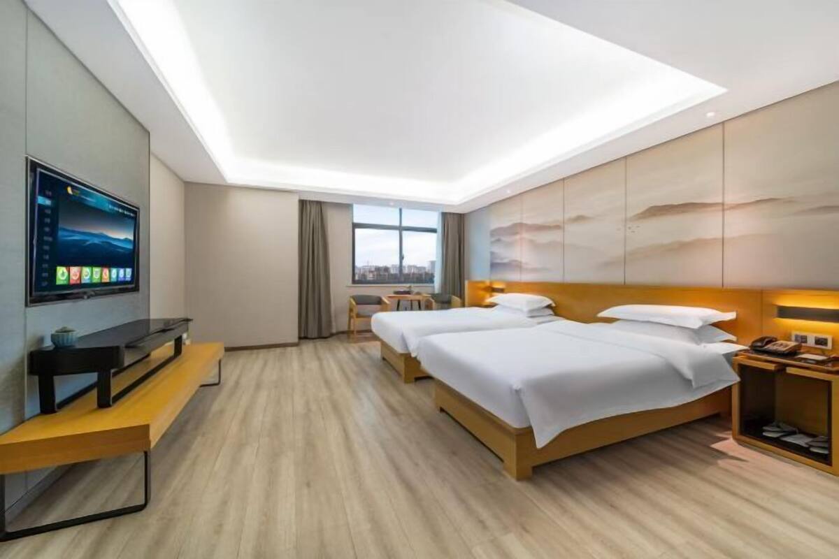 Habitación de hotel con dos camas, televisión, escritorio y ventana con vista a la ciudad.