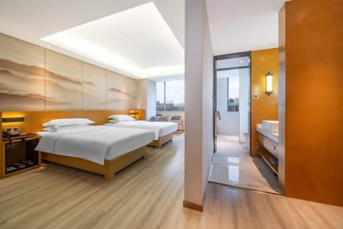Una habitación de hotel moderna con dos camas, suelo de madera, vistas a la ciudad y vestidor.