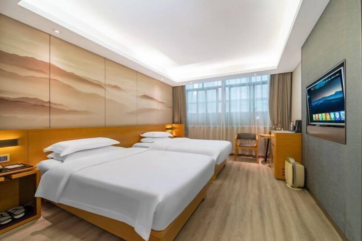 Habitación de hotel con dos camas, un escritorio, una silla, un televisor y un ventanal grande.