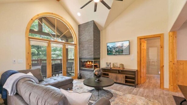 A spacious living room with a fireplace, a large arched window, and a ceiling fan. - 5 Bedroom Luxury Townhome Near Snowflake Lift in Breckenridge - Walk to Lift! (Breckenridge)