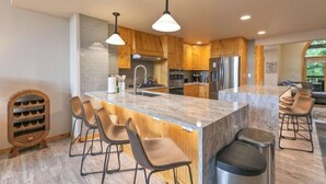 A modern kitchen with wooden cabinets, a marble island, and bar stools. - 5 Bedroom Luxury Townhome Near Snowflake Lift in Breckenridge - Walk to Lift! (Breckenridge)