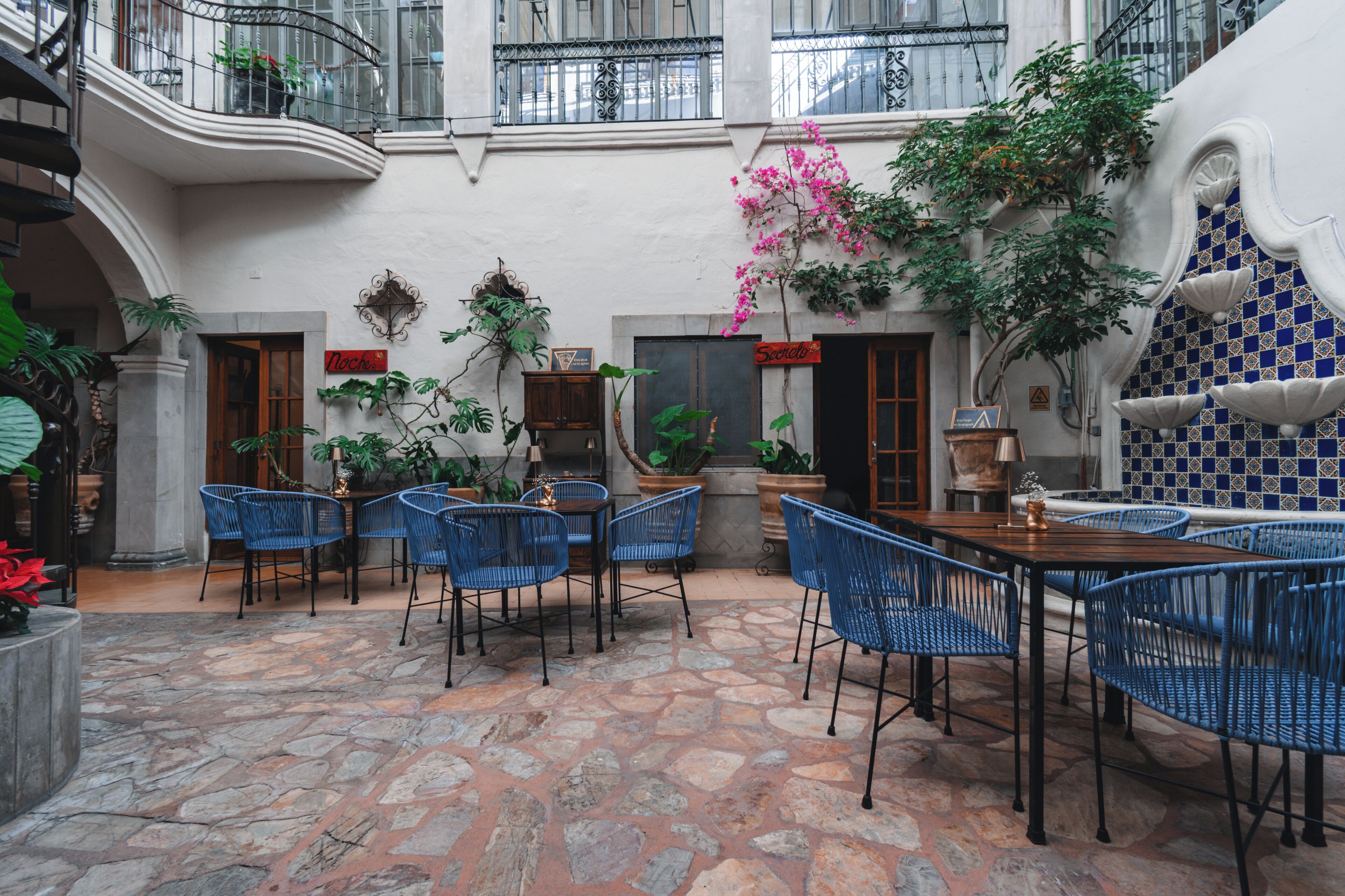 Un patio con suelo de piedra, sillas azules y plantas en macetas.