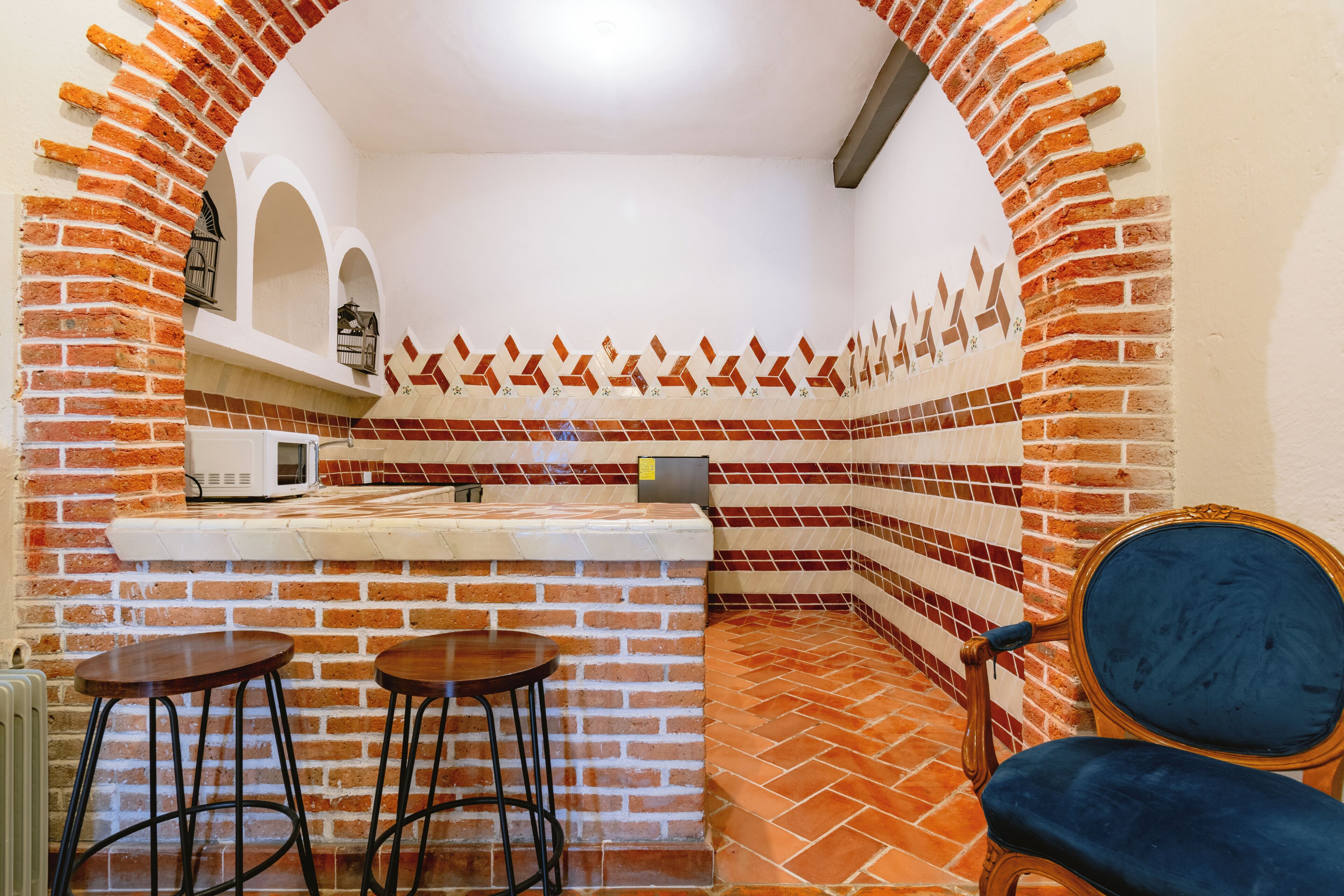 Una cocina con pared de ladrillo, salpicadero de azulejos, encimera blanca y dos taburetes.