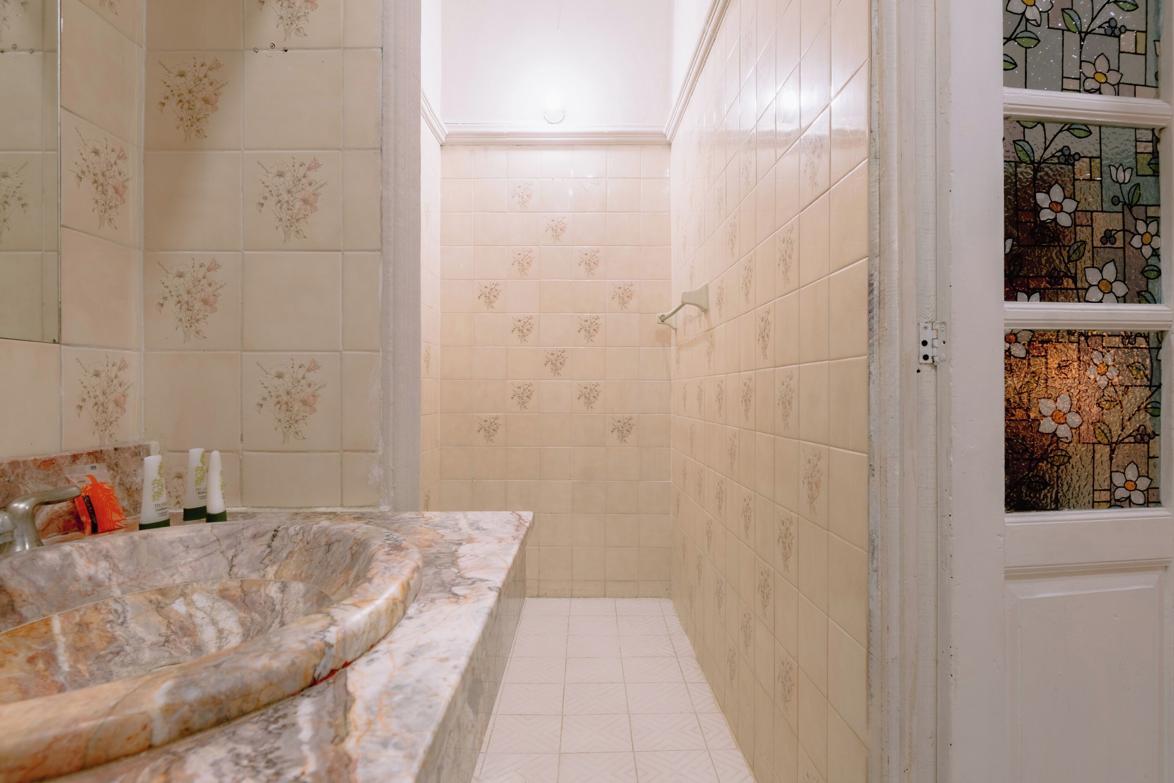Un baño con lavamanos de mármol, azulejos florales y una ventana con vitrales.