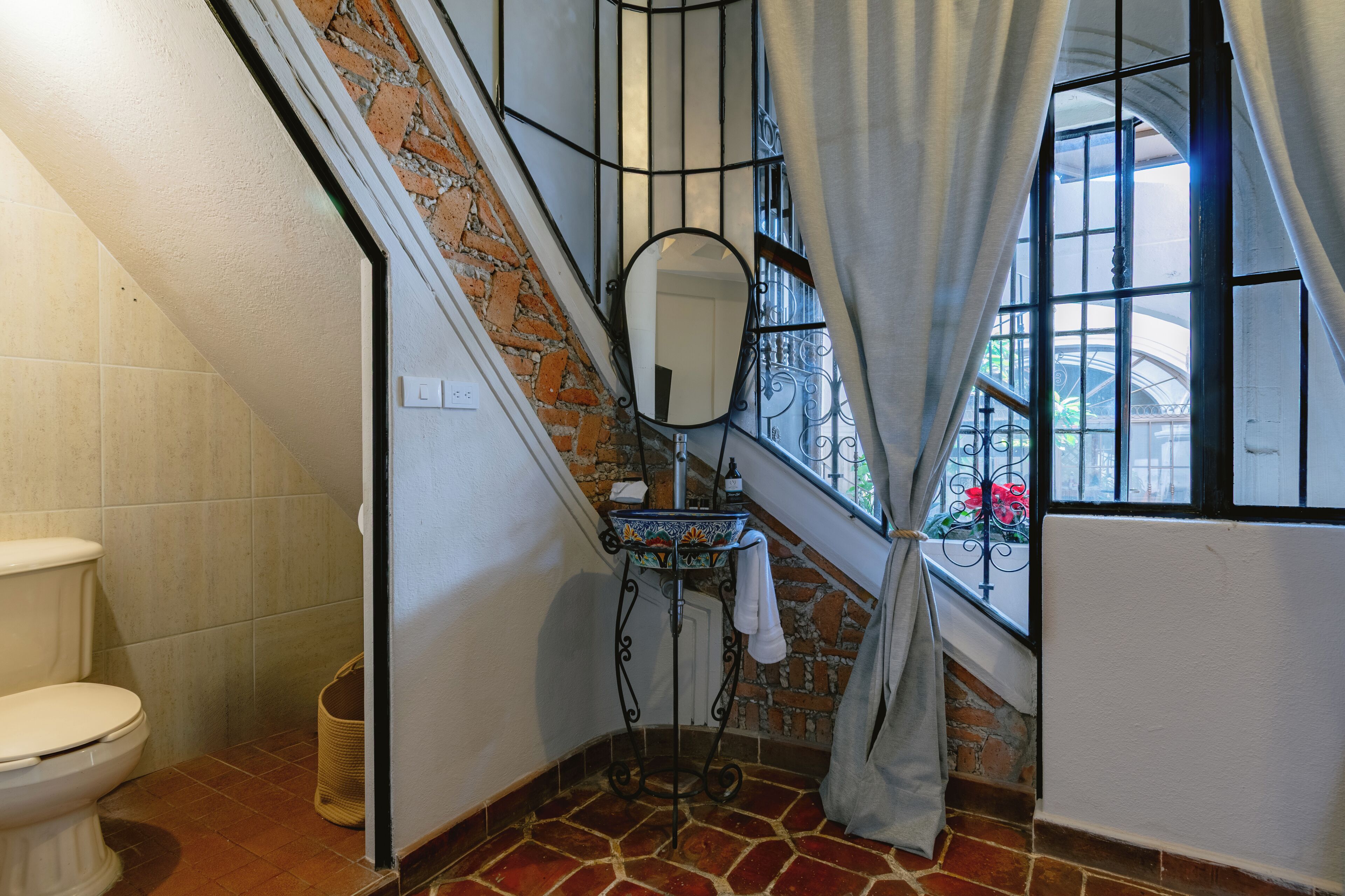 Une salle de bain avec des toilettes, un lavabo avec un miroir et une fenêtre avec des rideaux.